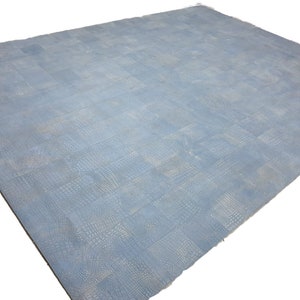 Könnte beinhalten: Ein hellblauer Teppich mit Krokodilledermuster. Der Teppich ist aus einem weichen, strukturierten Material gefertigt und hat einen dezenten Glanz.