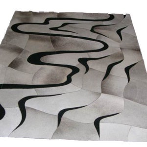 Può includere: Un tappeto in patchwork bianco e nero con un design ondulato. Il tappeto è in pelle di mucca e ha un aspetto moderno e astratto.
