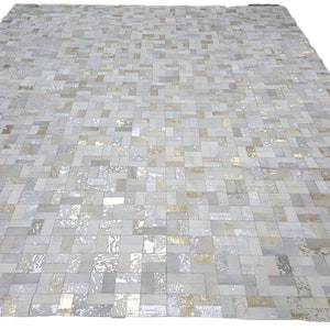 May include: A white and gold patchwork rug made of leather squares. The rug has a subtle sheen and a geometric pattern.