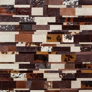 Puede incluir: Una alfombra de patchwork hecha de diferentes piezas de cuero de colores. La alfombra está compuesta por piezas rectangulares de cuero en tonos marrones, blancos y negros. Las piezas de cuero están dispuestas en un patrón de ladrillo.