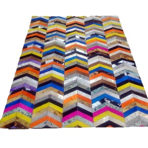 May include: A colourful chevron patterned rug made from leather. The rug is made up of various colours including orange, yellow, blue, pink, and silver.
