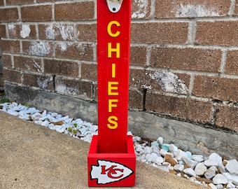 May include: A red wooden bottle opener with a white bottle opener and a yellow "CHIEFS" inscription. The bottom of the bottle opener has a red and white Kansas City Chiefs logo.