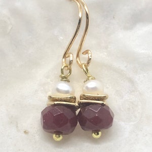 Peut inclure: Boucles d'oreilles pendantes en or avec une pierre précieuse facetée bordeaux et un accent de perle blanche.