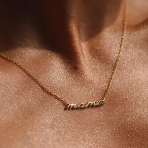 May include: A gold necklace with the word "mama" spelled out in cursive script.
