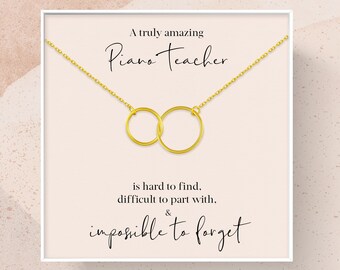 May include: A white card with a gold necklace featuring two interlocking circles. The card reads "A truly amazing Piano Teacher is hard to find, difficult to part with, & impossible to forget."