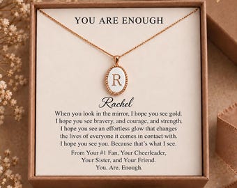 May include: A gold-toned necklace with an oval pendant featuring the letter R, presented in a box with the text YOU ARE ENOUGH, Rachel, and a message about bravery, courage, and strength, signed from your number one fan, cheerleader, sister, and friend.