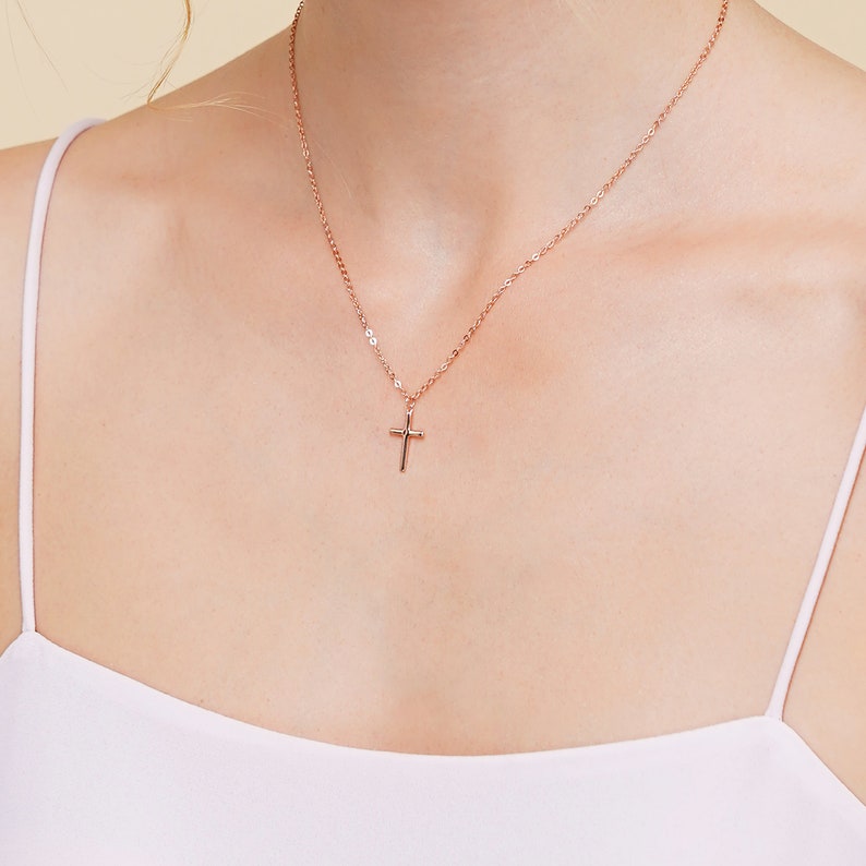 May include: A delicate rose gold chain necklace with a small cross pendant.