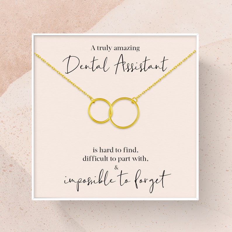 May include: A white card with a gold necklace featuring two interlocking circles. The card reads "A truly amazing Dental Assistant is hard to find, difficult to part with, & impossible to forget."