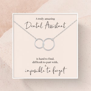 May include: A white card with a silver necklace featuring two interlocking circles. The card reads "A truly amazing Dental Assistant is hard to find, difficult to part with, & impossible to forget."