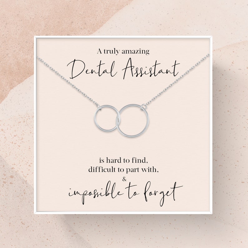 May include: A white card with a silver necklace featuring two interlocking circles. The card reads "A truly amazing Dental Assistant is hard to find, difficult to part with, & impossible to forget."