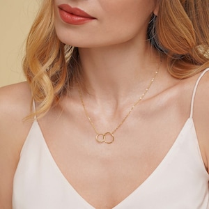 May include: A gold chain necklace with two interlocking circles as a pendant.