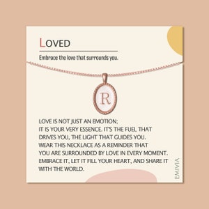 May include: Rose gold necklace with an oval pendant featuring the letter "R" on a white background. The pendant is on a chain, and the card reads "LOVED" and "Embrace the love that surrounds you."