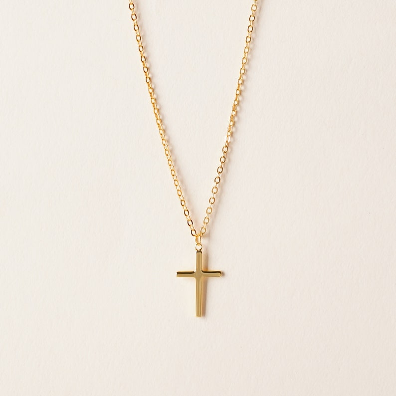 May include: A gold chain necklace with a simple gold cross pendant.