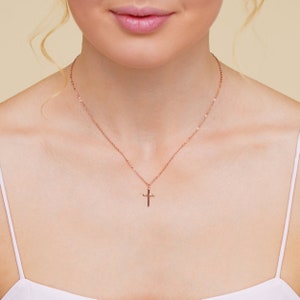 May include: A rose gold chain necklace with a small rose gold cross pendant.