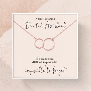 May include: A white card with a rose gold necklace featuring two interlocking circles. The card reads "A truly amazing Dental Assistant is hard to find, difficult to part with, & impossible to forget."