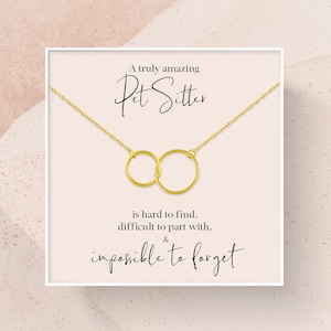May include: A white card with gold lettering that reads "A truly amazing Pet Sitter is hard to find, difficult to part with, & impossible to forget". A gold necklace with two interlocking circles hangs from the top of the card.