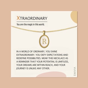 May include: A gold necklace with a pendant featuring the letter "R" in a white oval with a gold border. The necklace is on a white card with the text "XTRAORDINARY You are the magic in this world." and a message about defying expectations and redefining possibilities.