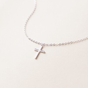 May include: A silver chain necklace with a small silver cross pendant.