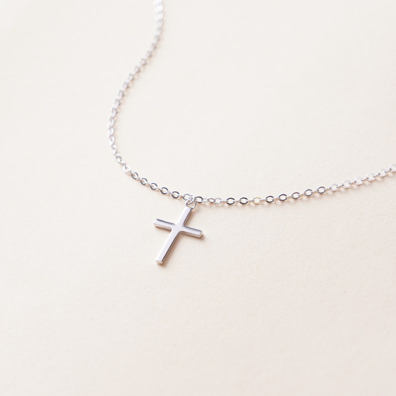 May include: A silver chain necklace with a small silver cross pendant.