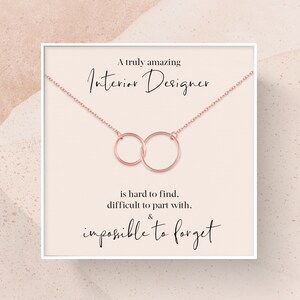 May include: A white card with a rose gold necklace featuring two interlocking circles. The card reads "A truly amazing Interior Designer is hard to find, difficult to part with, & impossible to forget."