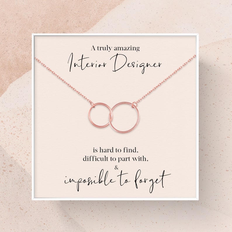 May include: A white card with a rose gold necklace featuring two interlocking circles. The card reads "A truly amazing Interior Designer is hard to find, difficult to part with, & impossible to forget."