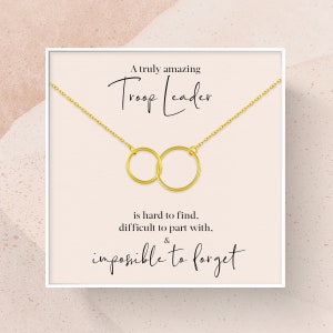 May include: A gold-colored necklace with two interlocking circles, presented on a card with the text "A truly amazing Troop Leader is hard to find, difficult to part with, & impossible to forget."