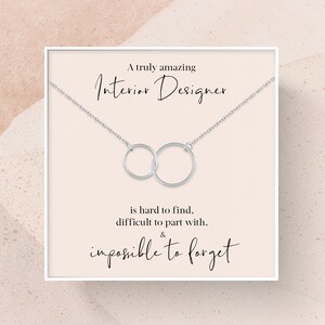 May include: A white card with a silver necklace featuring two interlocking circles. The card reads "A truly amazing Interior Designer is hard to find, difficult to part with, & impossible to forget."
