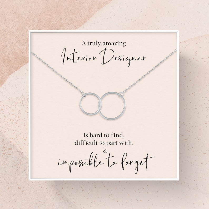 May include: A white card with a silver necklace featuring two interlocking circles. The card reads "A truly amazing Interior Designer is hard to find, difficult to part with, & impossible to forget."