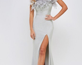 May include: A silver sparkly strapless maxi dress with a feather trim at the neckline and a thigh-high slit. The dress is fitted and has a long, flowing skirt.