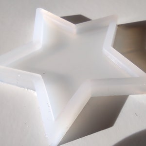 Può includere: Uno stampo in silicone bianco a forma di stella a cinque punte. Lo stampo ha un bordo rialzato attorno al perimetro.