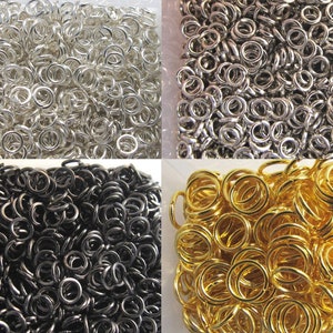 Op de afbeelding: Een assortiment metalen verbindingsringen in zilver, gunmetal, zwart en goud. De ringen zijn dicht op elkaar gepakt, waardoor een textuur ontstaat. Deze ringen worden vaak gebruikt bij het maken van sieraden en knutselprojecten.