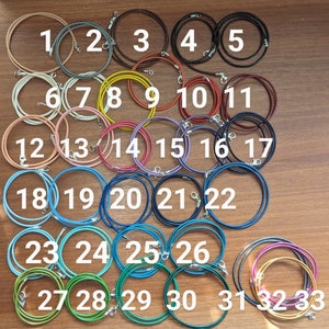 Pode incluir: Trinta e três cordões de couro em várias cores, numerados de 1 a 33. Os cordões estão dispostos em filas sobre uma superfície de madeira.
