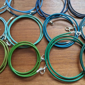 Könnte beinhalten: Sortiment an Lederkordeln in Blau- und Grüntönen. Jede Kordel ist mit einem silbernen Verschluss versehen.