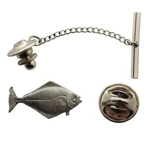 May include: Silver-toned pewter tie tack featuring a detailed halibut fish design. The tie tack has a safety pin clasp and a chain with a bar.