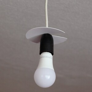 May include: A white ceiling light fitting with a white cord and a white plastic canopy. A white LED light bulb is attached to the fitting.