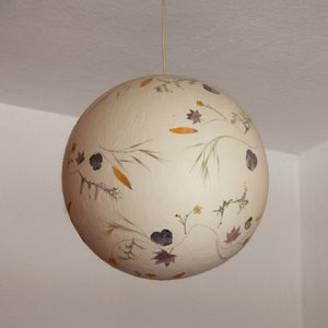 May include: A white spherical lampshade with dried flowers and leaves pressed into the surface.