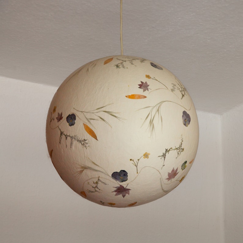 May include: A white spherical lampshade with dried flowers and leaves pressed into the surface.