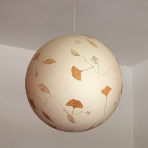 May include: A white sphere pendant light with dried leaves and flowers pressed into the surface.