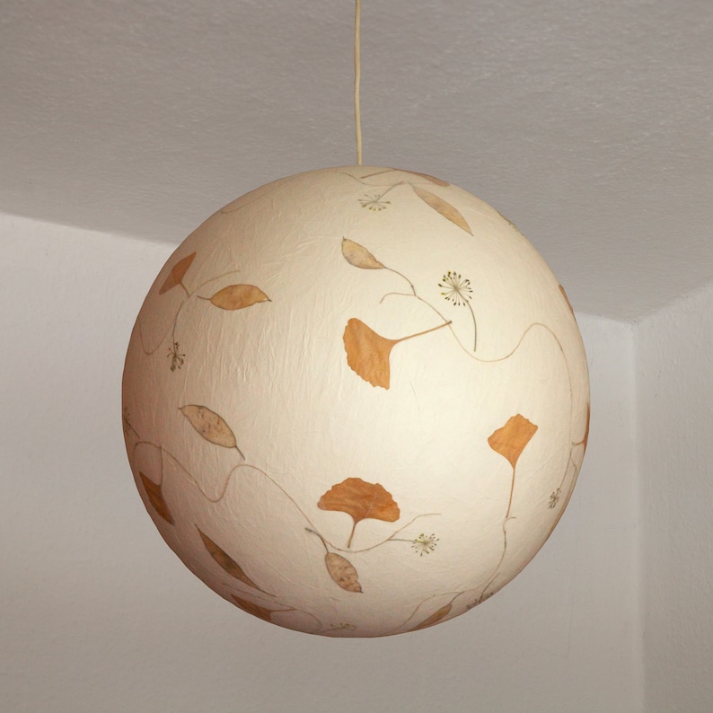 May include: A white sphere pendant light with dried leaves and flowers pressed into the surface.