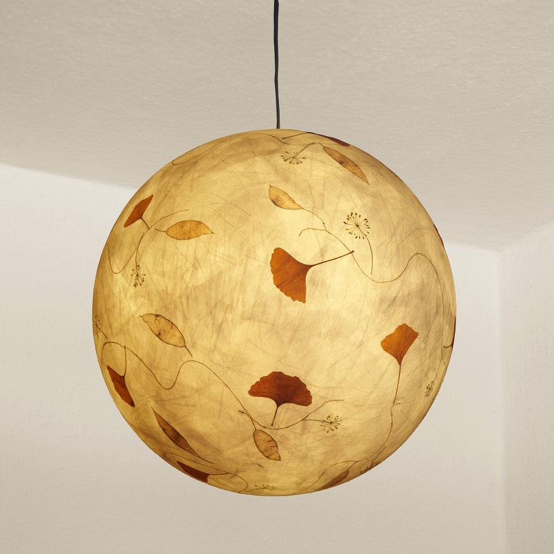 May include: A round, cream-colored pendant light with a delicate pattern of brown leaves and vines. The light is suspended from a black cord.