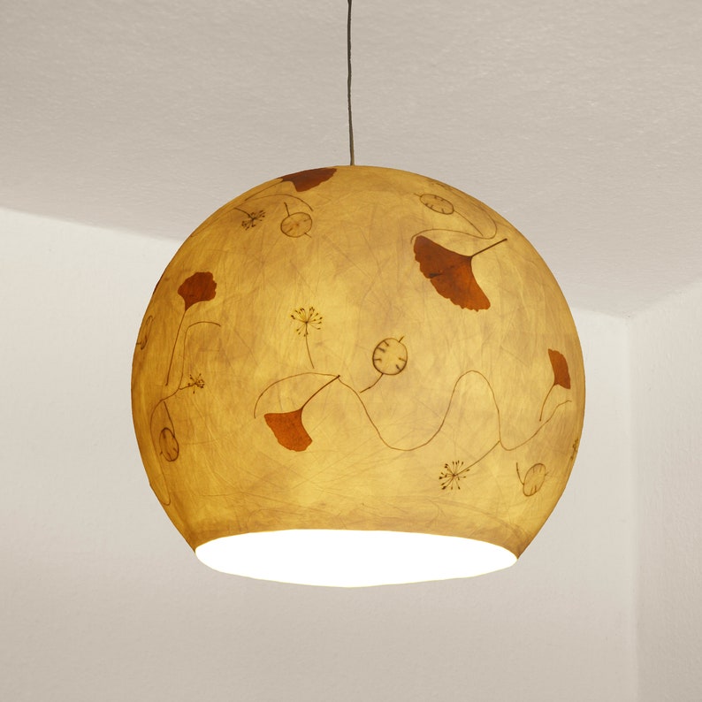 May include: A round, yellow pendant light with a white interior and a brown floral design. The light is hanging from a white ceiling.
