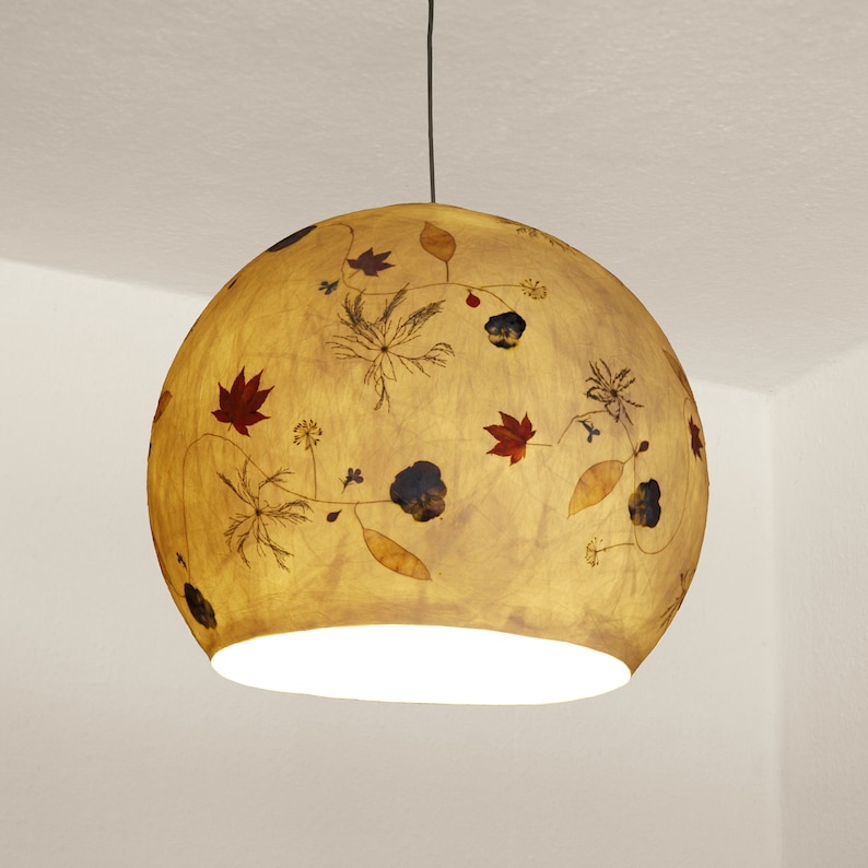 May include: A round, beige pendant light with a white interior. The light features a floral design with pressed leaves and flowers in shades of brown, red, and yellow.