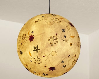 May include: A round, cream-colored pendant light with a black cord. The pendant light is made of paper and has a floral design with pressed flowers and leaves.