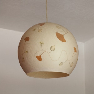 May include: A white round pendant light with a textured surface and a design of brown pressed leaves and flowers.
