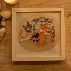 Peut inclure: Une illustration encadrée d'une personne assise sur le sol avec un chat. La personne porte un pull orange et a les cheveux roux. Le chat est blanc et orange. Il y a des plantes en arrière-plan.