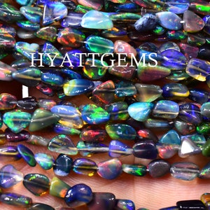 Könnte beinhalten: Stränge aus schillernden schwarzen Opalperlen in verschiedenen Farben, darunter Blau, Grün und Rot. Die Perlen sind unregelmäßig geformt und aufgefädelt. Der Text "HYATTGEMS" ist sichtbar.