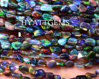 Könnte beinhalten: Stränge aus schillernden schwarzen Opalperlen in verschiedenen Farben, darunter Blau, Grün und Rot. Die Perlen sind unregelmäßig geformt und aufgefädelt. Der Text "HYATTGEMS" ist sichtbar.