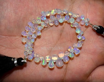May include: A strand of white opal teardrop beads with iridescent rainbow flashes. The beads are strung on a cord with black tassels at each end.