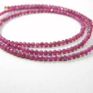 Könnte beinhalten: Eine Schnur aus rosa Rubinperlen, facettiert und auf einem dünnen Draht aufgefädelt. Die Perlen sind klein und gleichmäßig groß.