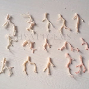 May include: A collection of 25 natural coral branches in various sizes and shapes. The coral is a pale pink color with some white branches. The coral is arranged on a white surface.